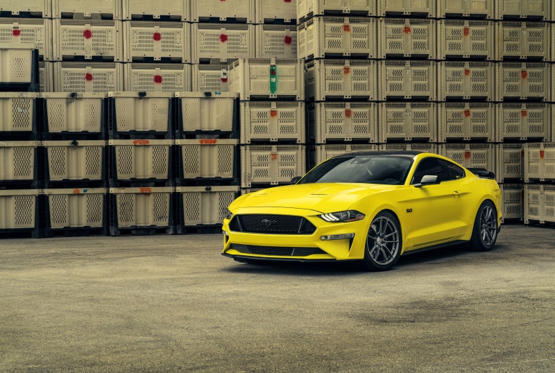 Yellow Ford Mustang parked in front of stacked crates