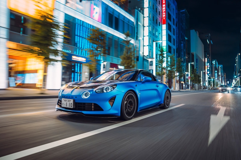 Blue Alpine A110 driving through a city at night