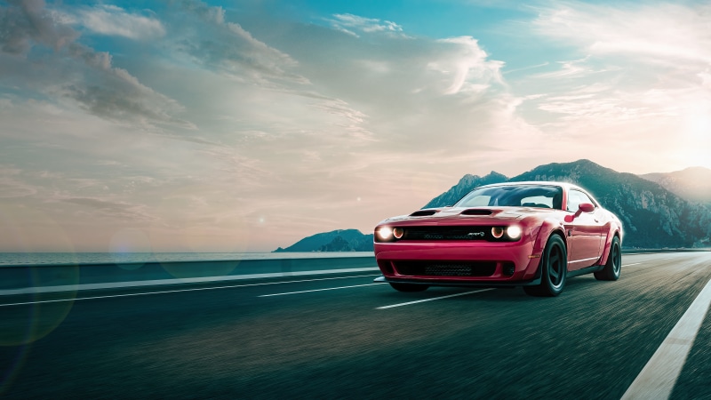Red Dodge Challenger driving on a coastal road