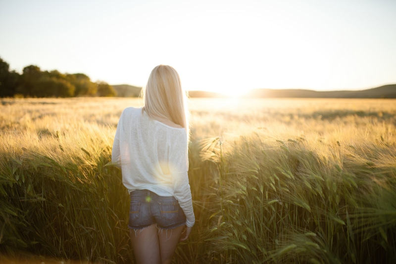 Woman in denim shorts in a wheat field at sunset
