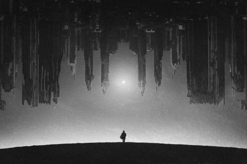 Monochrome artwork of a person facing an inverted cityscape