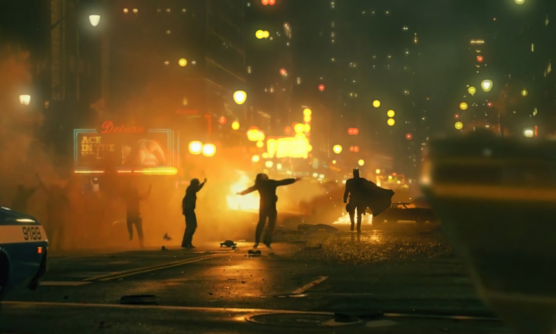 Batman in a burning city street with rioters