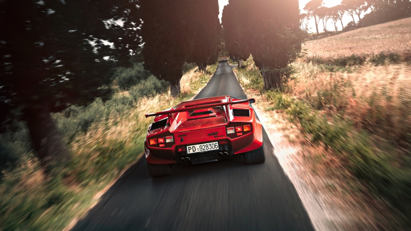 Red Lamborghini Countach driving on a tree-lined road