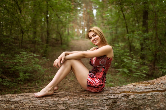 Smiling Woman Sitting on Tree Trunk in Forest