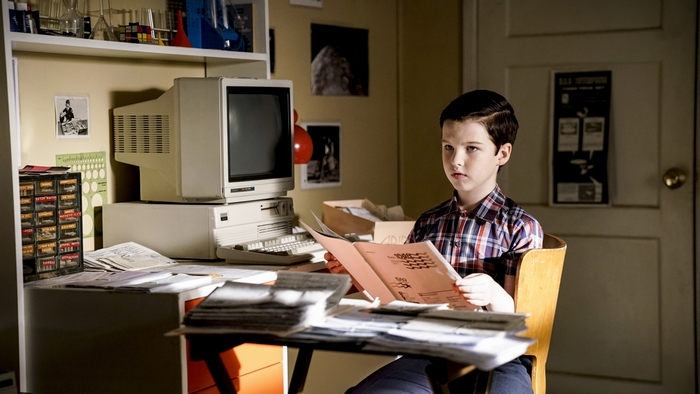 Young Sheldon studying at his desk with a vintage computer