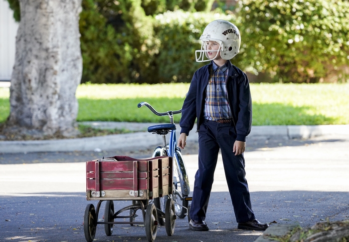 Young Sheldon in football helmet with bike and wagon