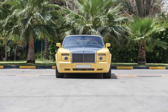 Yellow Rolls-Royce Phantom luxury car among palm trees