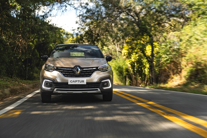 Gold Renault Captur SUV driving on a scenic road.