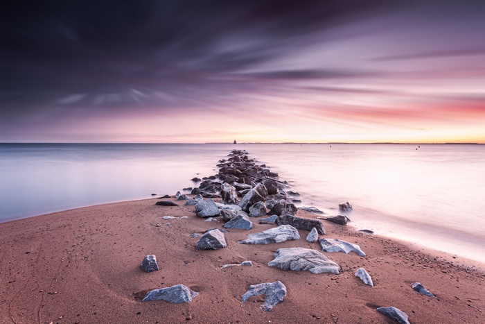 Colorful sunset over ocean with rocky path to horizon