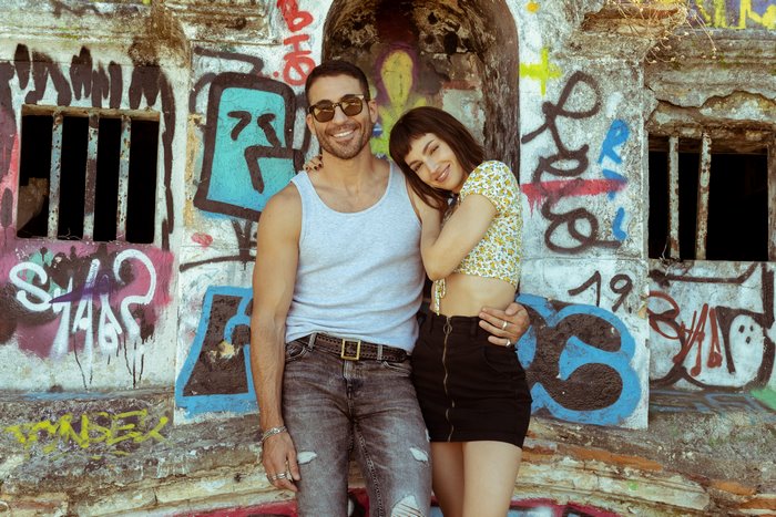 Úrsula Corberó and Miguel Herrán smiling by graffiti wall