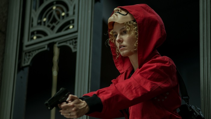 Stockholm in red jumpsuit and Dali mask holding a gun