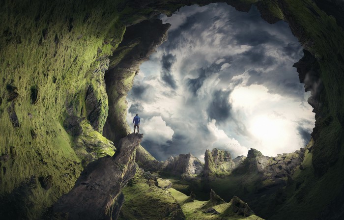 Man in mossy cave looking out at spiral sky