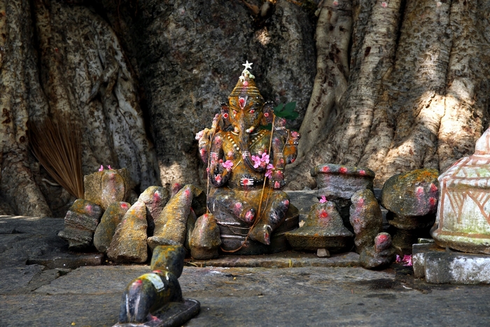 Hindu Ganesh statue adorned with flowers under a tree