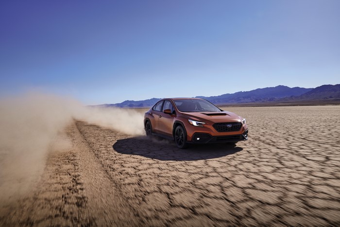 Orange Subaru WRX sport car kicking up dust in desert