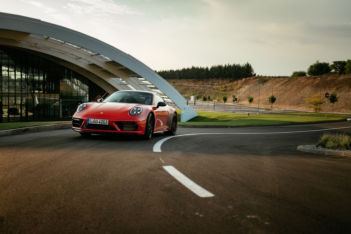 Red Porsche 911 Carrera GTS driving past modern building