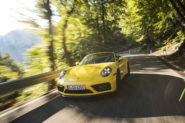 Yellow Porsche 911 Cabriolet speeding on a sunny forest road