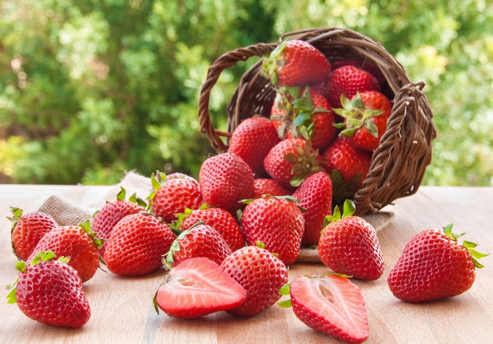 Fresh strawberries spilled from a basket on a wooden table