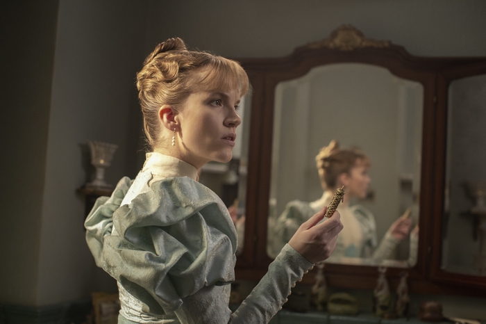 Imogen Spurnrose holding ornate object, reflected in mirror