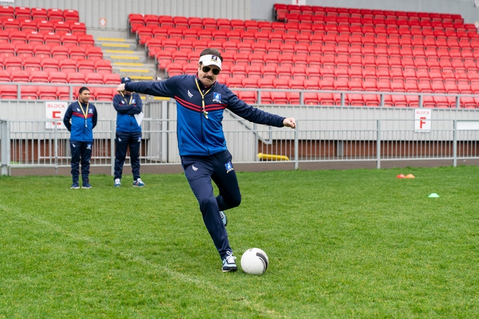 Ted Lasso kicking soccer ball on field