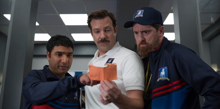 Ted Lasso coaches examining an orange paper object