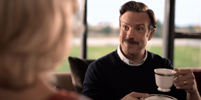 Ted Lasso holding a teacup with a curious expression