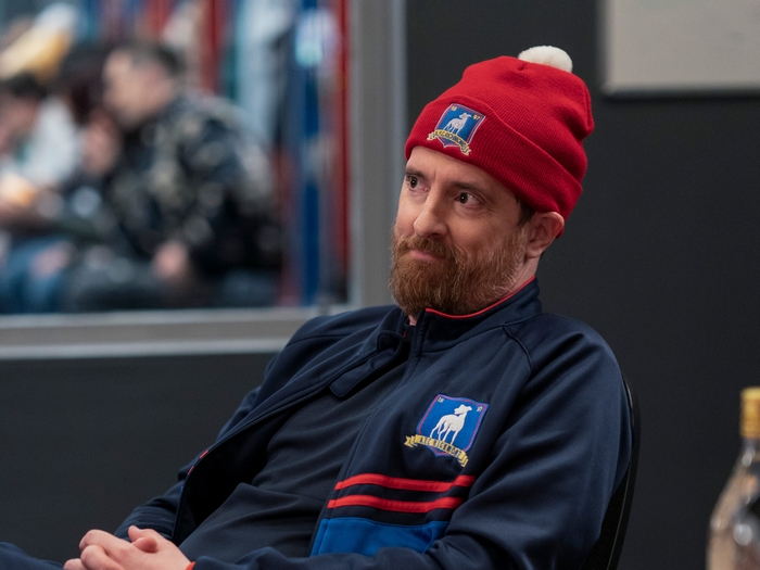 Brendan Hunt as Coach Beard wearing a red beanie