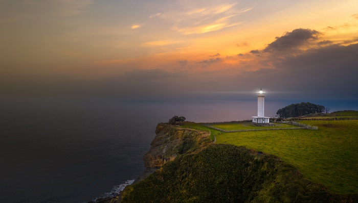 Lighthouse Shining at Dusk on a Coastal Cliff