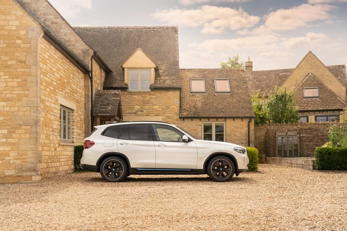White BMW iX3 electric SUV parked at a stone house
