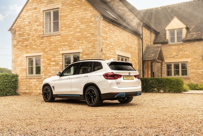 White BMW iX3 electric SUV parked at a stone house