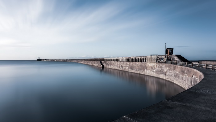 Long exposure of a curved concrete dam and calm water