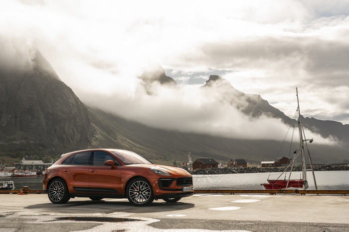 Orange Porsche Macan S on a pier with cloudy mountains