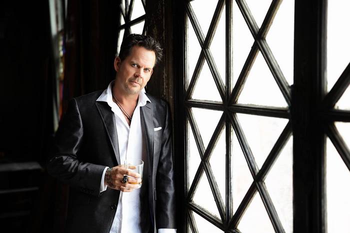 Gary Allan in a suit holding a drink by a window