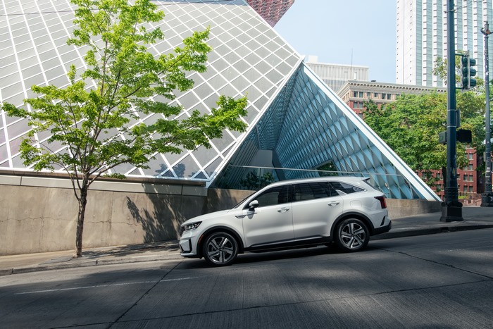 White Kia Sorento PHEV SUV by modern glass building