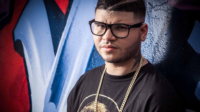 Farruko in glasses and gold chains against graffiti wall