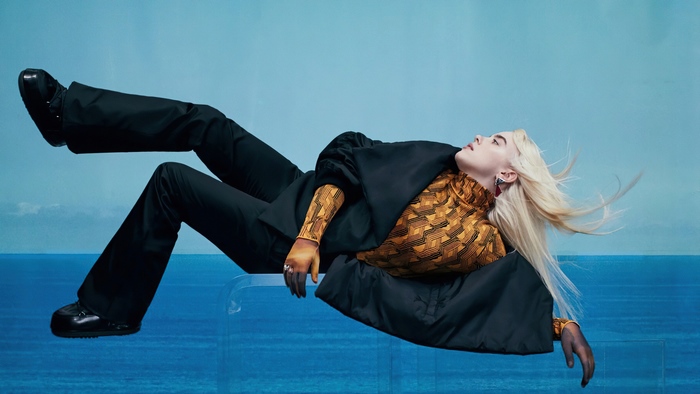 Blonde Billie Eilish suspended against blue sky and water