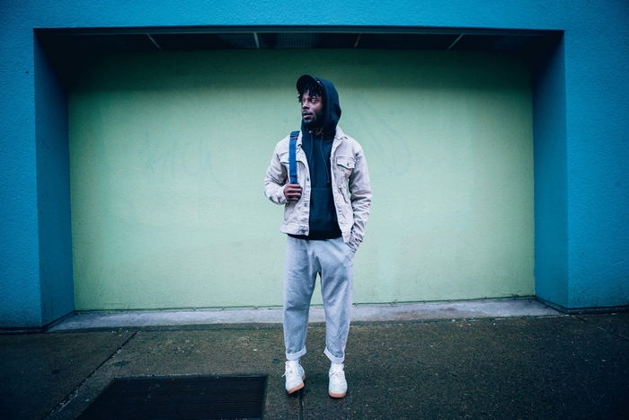 Isaiah Rashad posing against a blue and green wall