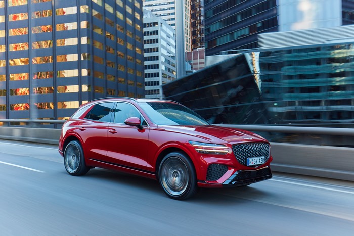 Red Genesis GV70 SUV driving through a city