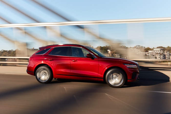 Red Genesis GV70 SUV driving fast on a bridge