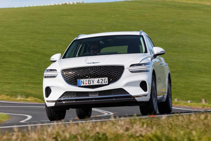 White Genesis GV70 SUV driving on a winding road
