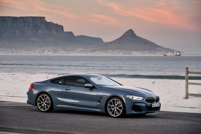 BMW M850i luxury car by the ocean and mountains at sunset