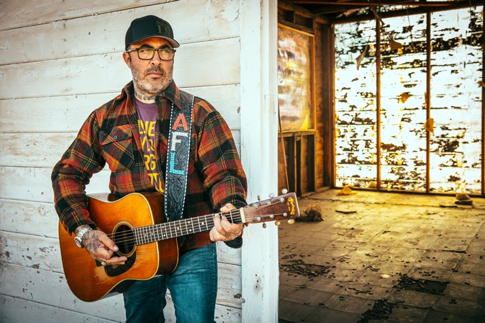 Aaron Lewis playing acoustic guitar in a rustic setting