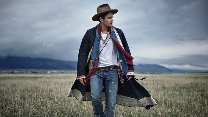 John Mayer in a field under a dramatic cloudy sky