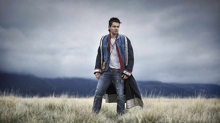 John Mayer standing in a field under a cloudy sky