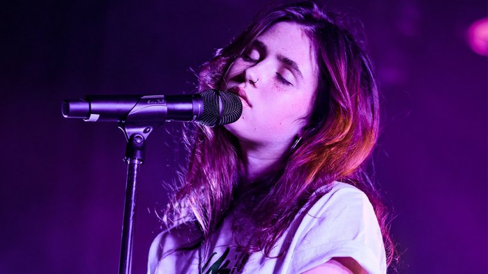 Clairo singing passionately on stage under purple lights