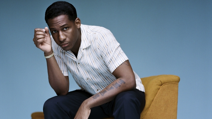Leon Bridges sitting on yellow chair against blue background