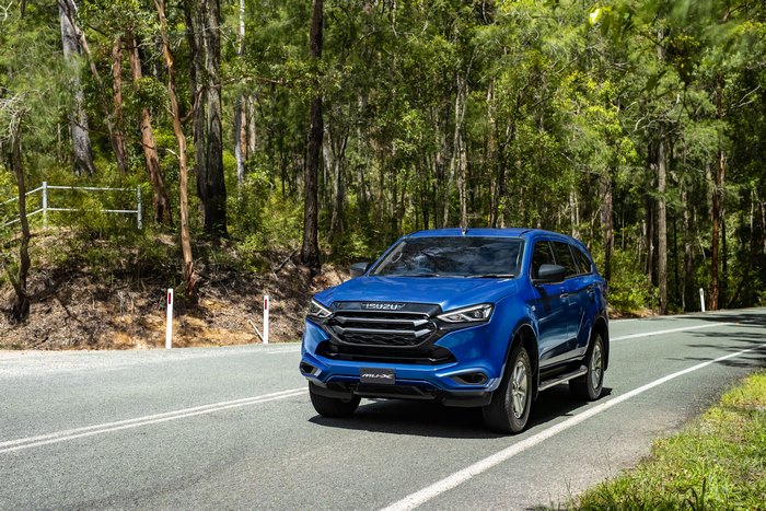Blue Isuzu MU-X SUV on a scenic forest road