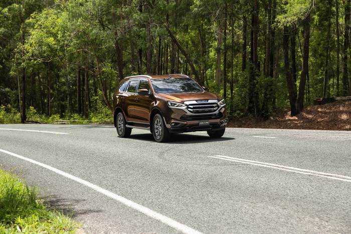 Brown Isuzu MU-X SUV on a road surrounded by trees