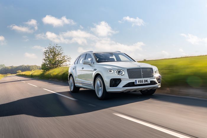 White Bentley Bentayga Hybrid SUV driving on a road.