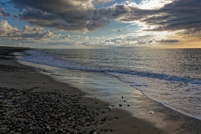 Dramatic Clouds and Sunset Glow over a Pebble Beach