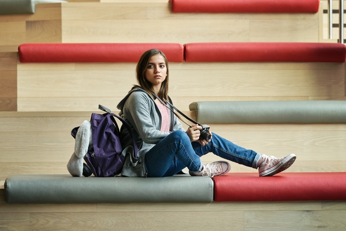 Isabela Merced looking serious with camera and backpack